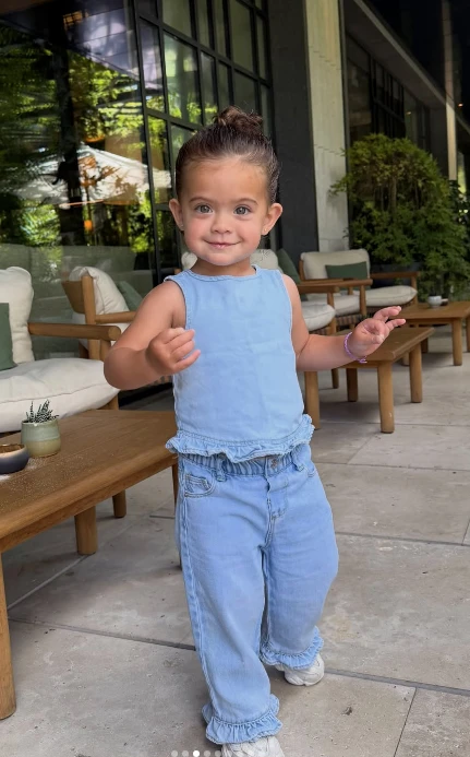 Olivia, la hija de Sergio “Kun” Agüero y Sofía Calzetti, volvió a conquistar con uno de sus looks. Esta vez, lució un conjunto de jean celeste que reúne comodidad, frescura y uno de los detalles que gana protagonismo en la moda: los volados.

La pequeña llevó una remera sin mangas y un pantalón amplio confeccionados en denim liviano. Ambas prendas incorporan terminaciones con volados, el recurso encargado de transformar el clásico total look de jean en una propuesta mucho más romántica.

Olivia se sumó a la tendencia del “denim romántico”

El denim romántico propone suavizar la estética urbana y descontracturada del jean mediante detalles delicados como volados, bordados, lazos, frunces y terminaciones onduladas.

En el look de Olivia, los volados aparecen en la cintura de la remera y en los ruedos del pantalón, generando movimiento y aportándole un aire divertido al conjunto.

La elección del mismo tono de jean en ambas prendas crea un efecto total denim o denim on denim, otra tendencia que continúa vigente y permite lograr un outfit coordinado sin demasiados elementos.

Las claves del look de Olivia

La parte superior presenta un diseño sin mangas, de líneas simples y con un pequeño volado en la terminación. El pantalón, en tanto, se destaca por su silueta holgada y cómoda, además de repetir el detalle de volados a la altura de los tobillos.

Para completar el outfit, Olivia llevó zapatillas blancas, un básico que acompaña la estética relajada del conjunto y permite que el denim sea el verdadero protagonista.

Su pelo recogido en un rodete alto terminó de darle al estilismo un toque fresco y práctico.

Cómo llevar la tendencia del jean con volados

Los volados ofrecen una forma original de renovar las prendas de jean y pueden aparecer en camisas, tops, vestidos, polleras, camperas o pantalones.

Para adoptar esta tendencia, se puede elegir una única prenda intervenida y combinarla con básicos neutros. Otra posibilidad es seguir la fórmula de Olivia y apostar por un conjunto coordinado, utilizando el mismo tono de denim de pies a cabeza.

sofia calzetti y el look de su hija Olivia