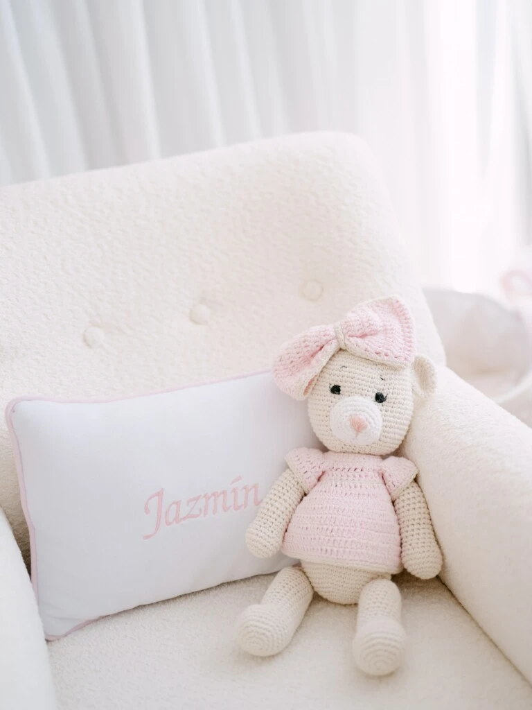 El asiento tiene un muñeco tejido y un almohadón blanco con el nombre Jazmín bordado en rosa, un detalle personalizado que refuerza la delicada paleta elegida para el ambiente.